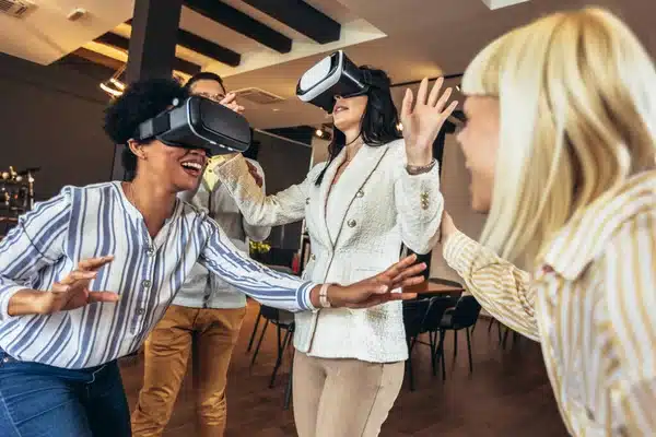 Quatre individus portant des casques de réalité virtuelle, exprimant leur enthousiasme devant un mur de briques, symbolisant une expérience immersive de teambuilding.